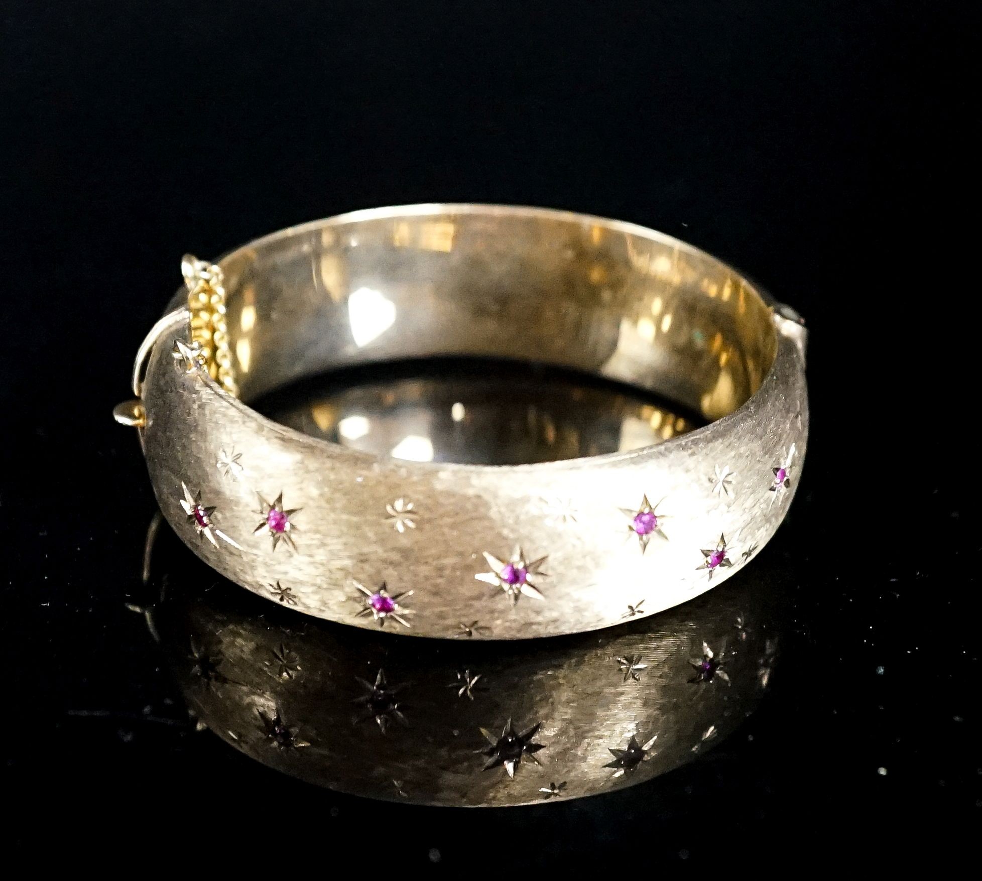 A 1960's engraved 9ct gold and ruby set hinged bracelet, interior diameter 58mm, gross weight 35.7 grams.